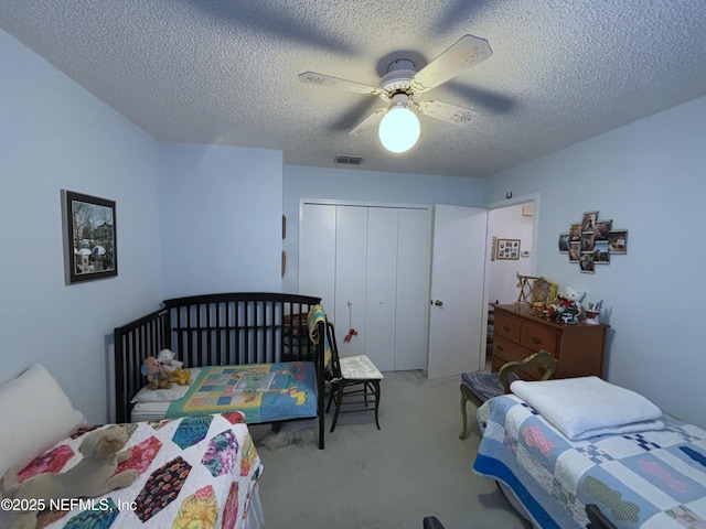 bedroom with a closet, visible vents, carpet flooring, ceiling fan, and a textured ceiling