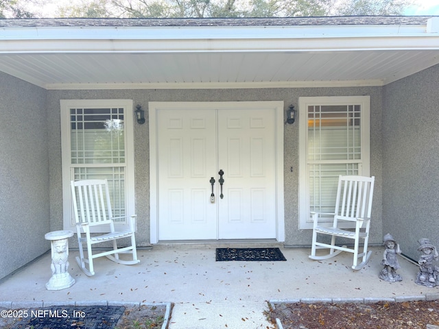 view of exterior entry with a porch and stucco siding