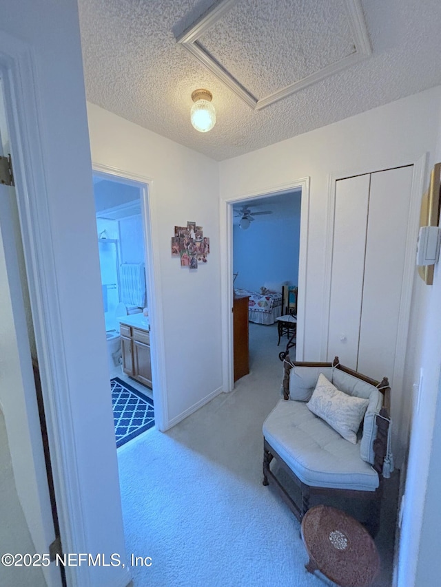 hallway with a textured ceiling, carpet flooring, and attic access