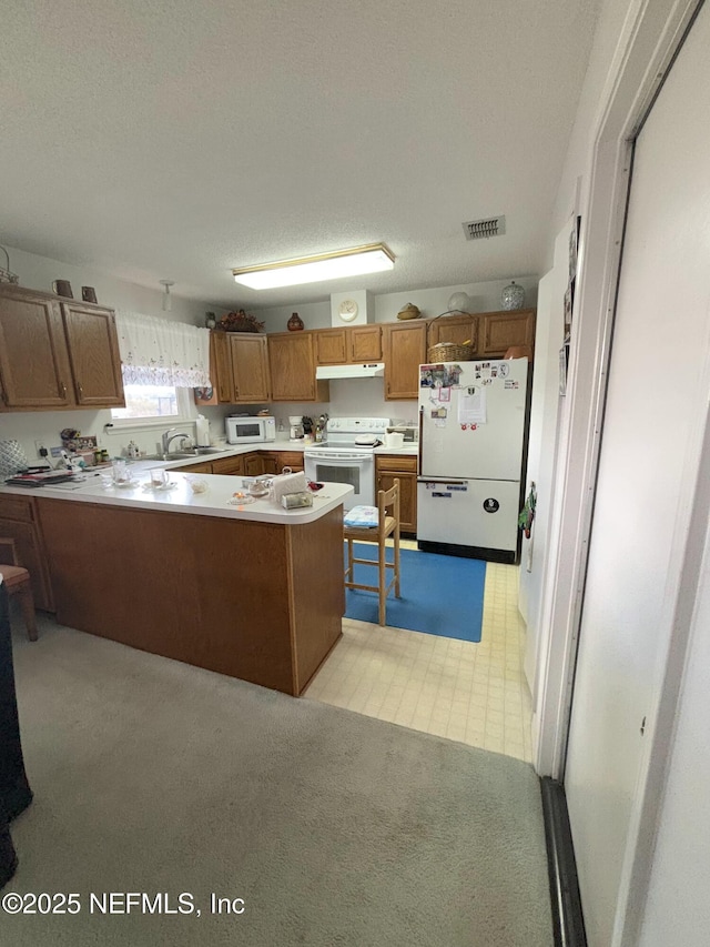 kitchen featuring white appliances, brown cabinets, a peninsula, light countertops, and under cabinet range hood