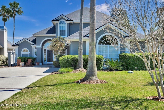 traditional home with a front lawn, roof with shingles, and stucco siding