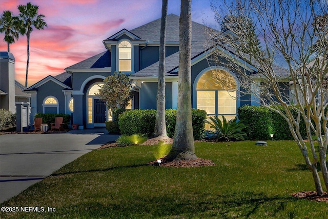 traditional-style house featuring stucco siding, a shingled roof, and a yard