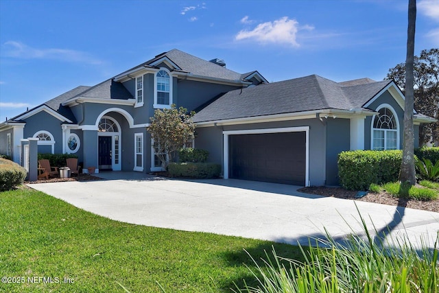 traditional home with stucco siding, a front lawn, concrete driveway, an attached garage, and a shingled roof