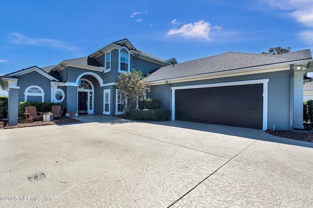 traditional home featuring stucco siding, an attached garage, roof with shingles, and driveway