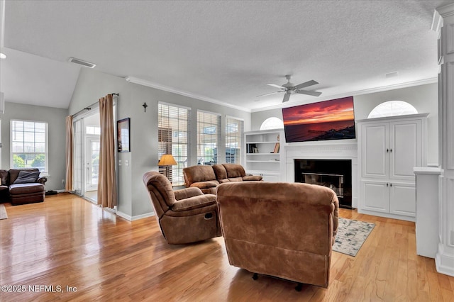 living room with a ceiling fan, visible vents, a fireplace, light wood-style floors, and a textured ceiling