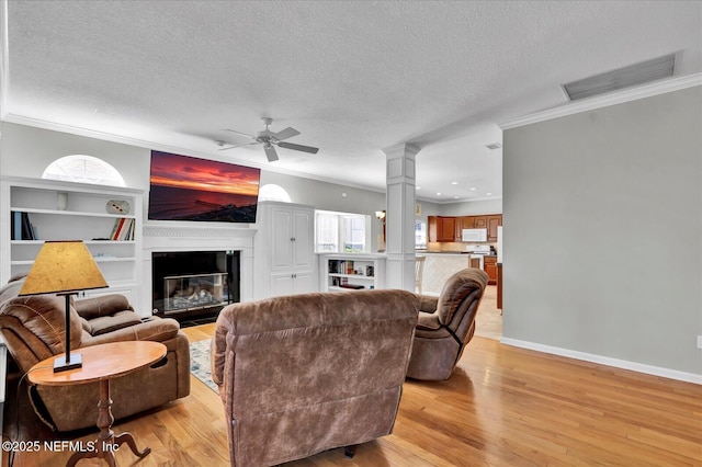 living room featuring light wood-type flooring, visible vents, ornamental molding, decorative columns, and ceiling fan