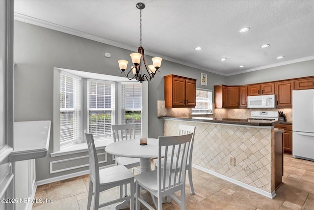 kitchen featuring dark countertops, backsplash, a chandelier, ornamental molding, and white appliances