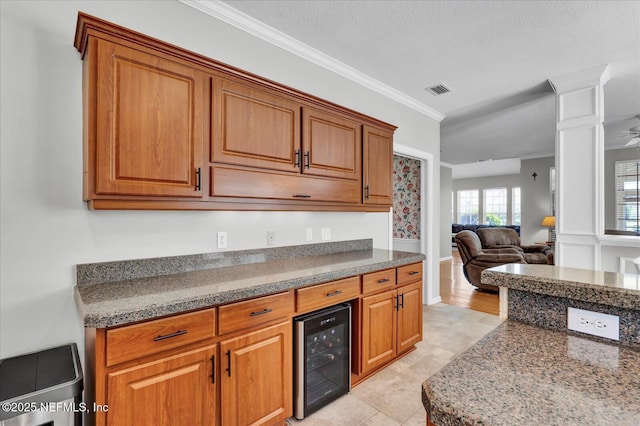 kitchen with beverage cooler, ornamental molding, dark stone countertops, open floor plan, and brown cabinetry