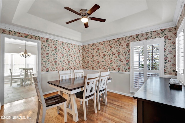 dining space with a wainscoted wall, a raised ceiling, and wallpapered walls