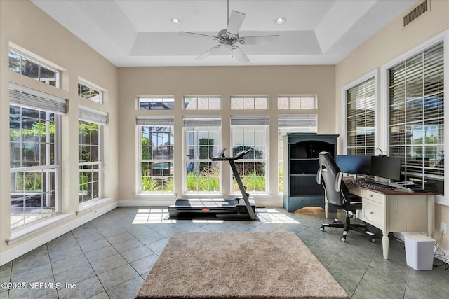 tiled office space with a tray ceiling, baseboards, visible vents, and a ceiling fan