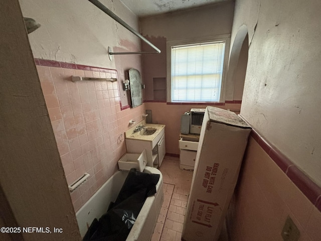 bathroom featuring shower / tub combination, tile walls, a sink, and wainscoting