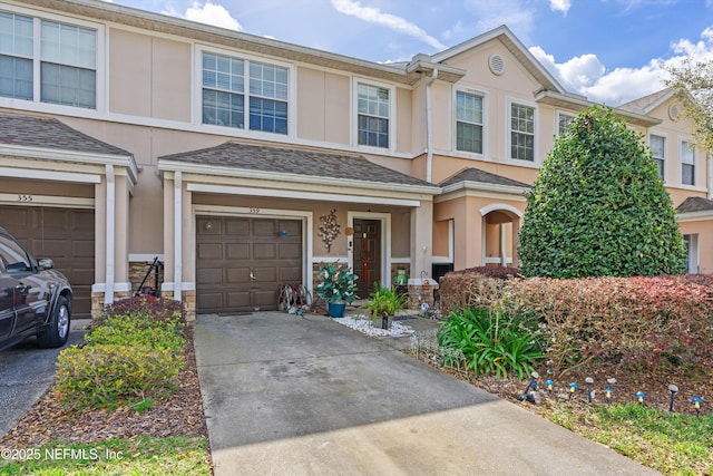 view of property featuring a shingled roof, driveway, an attached garage, and stucco siding