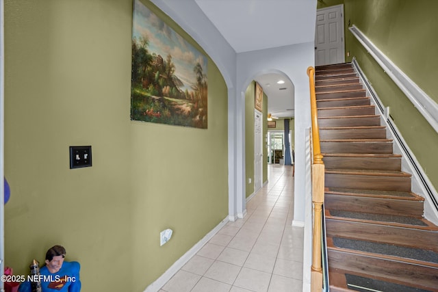 staircase featuring tile patterned flooring, arched walkways, and baseboards