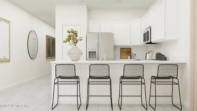 kitchen featuring a peninsula, white cabinetry, light countertops, white fridge with ice dispenser, and stainless steel microwave