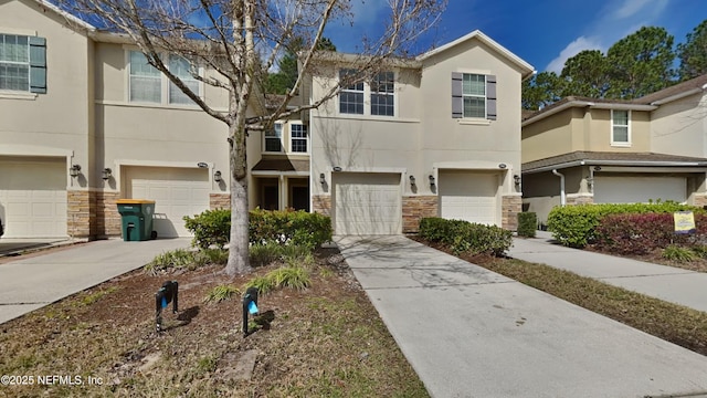 townhome / multi-family property with a garage, stone siding, concrete driveway, and stucco siding