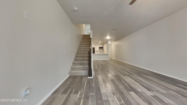 unfurnished living room featuring stairs, ceiling fan, wood finished floors, and baseboards