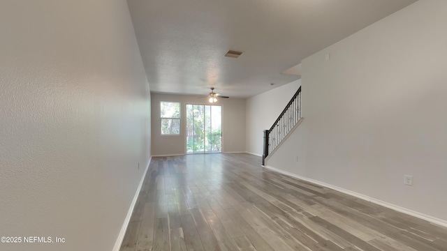 empty room featuring visible vents, stairway, ceiling fan, wood finished floors, and baseboards