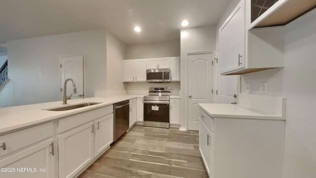 kitchen with light wood finished floors, appliances with stainless steel finishes, light countertops, white cabinetry, and a sink