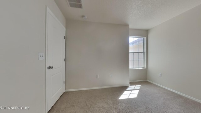 spare room featuring visible vents, light colored carpet, a textured ceiling, and baseboards