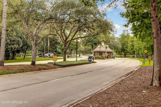 view of street featuring a gated entry, curbs, traffic signs, and street lighting