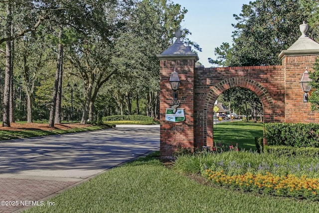 community / neighborhood sign featuring decorative driveway and a lawn