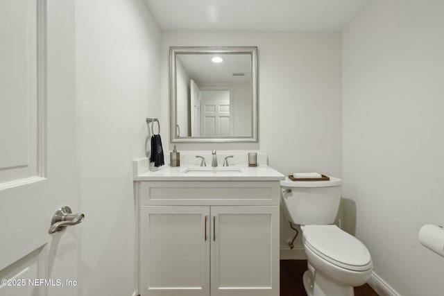 half bathroom with baseboards, toilet, and vanity