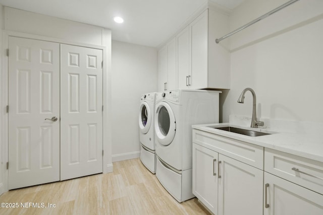 clothes washing area with baseboards, light wood-type flooring, washer and dryer, cabinet space, and a sink