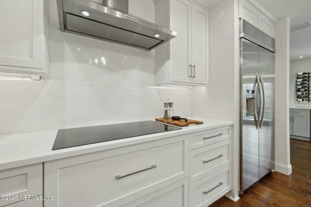 kitchen with range hood, dark wood-type flooring, black electric stovetop, tasteful backsplash, and stainless steel built in refrigerator