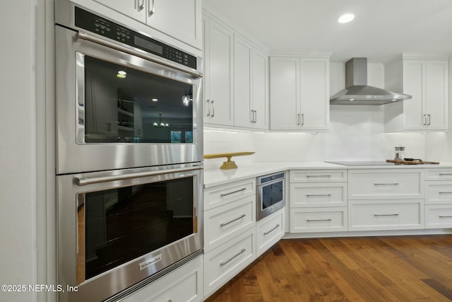 kitchen with double oven, white cabinets, wall chimney exhaust hood, and dark wood-style floors