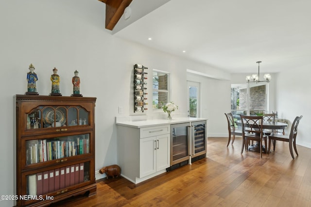 kitchen featuring beverage cooler, light countertops, an inviting chandelier, wood finished floors, and white cabinets