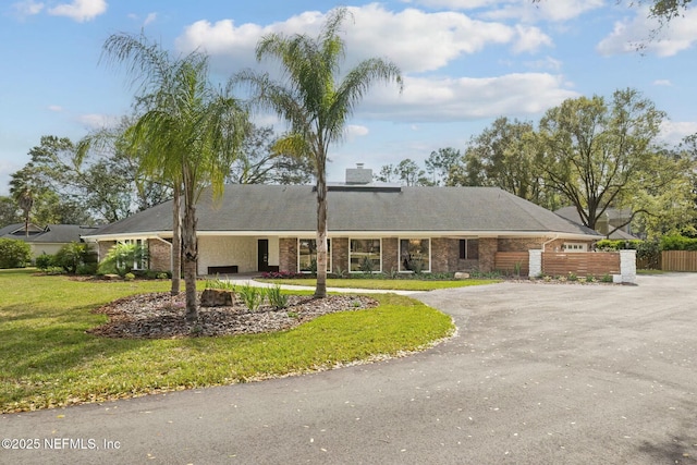 single story home featuring fence, a chimney, a front lawn, aphalt driveway, and brick siding