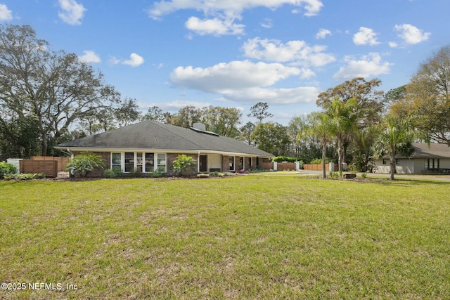 rear view of property featuring a lawn, brick siding, and fence