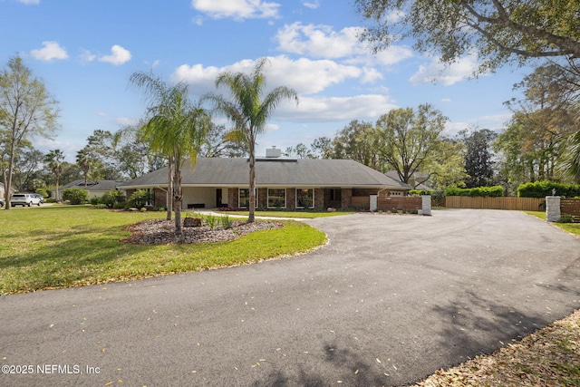 single story home with aphalt driveway, brick siding, a front lawn, and fence