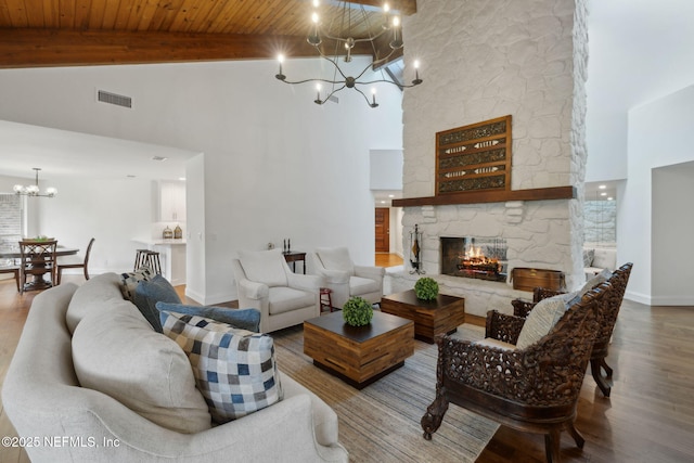 living room with wood finished floors, visible vents, a stone fireplace, beamed ceiling, and a notable chandelier