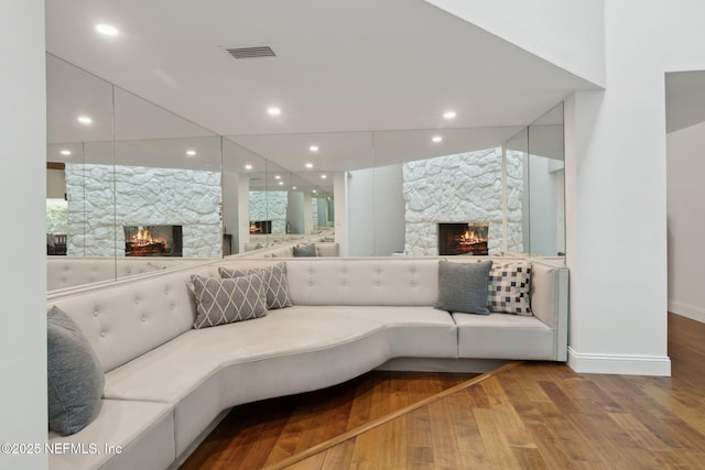 living room with recessed lighting, visible vents, a stone fireplace, and wood finished floors