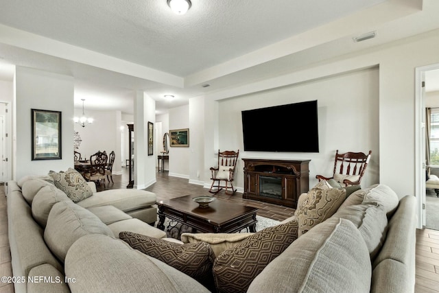 living room featuring a notable chandelier, a raised ceiling, visible vents, a glass covered fireplace, and wood finished floors