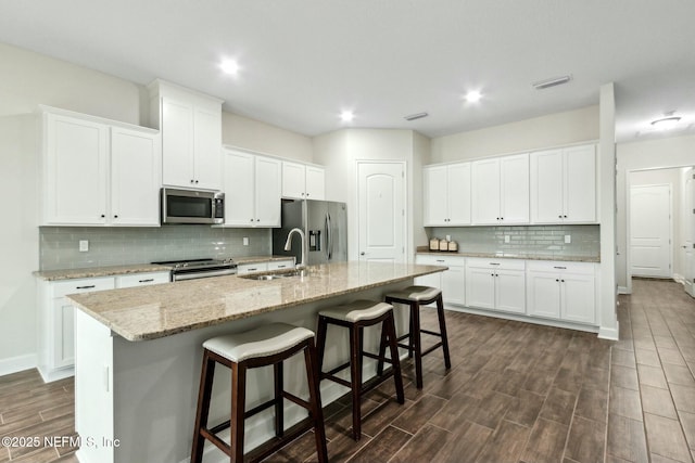 kitchen featuring a center island with sink, a breakfast bar area, appliances with stainless steel finishes, wood tiled floor, and a sink