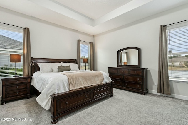 bedroom featuring a raised ceiling, light carpet, and baseboards