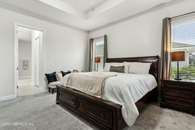 bedroom featuring a raised ceiling, light carpet, baseboards, and multiple windows