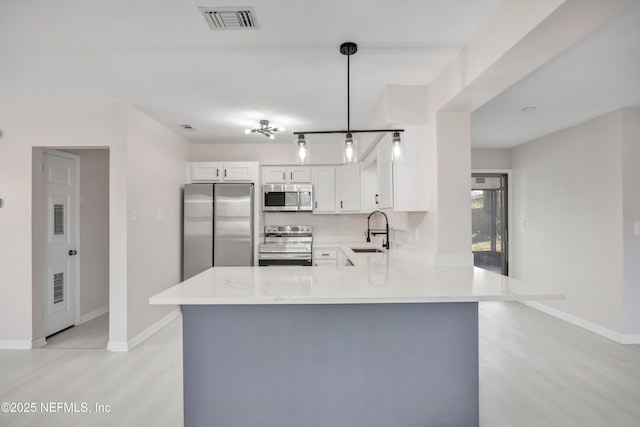 kitchen featuring visible vents, a peninsula, light stone countertops, stainless steel appliances, and a sink