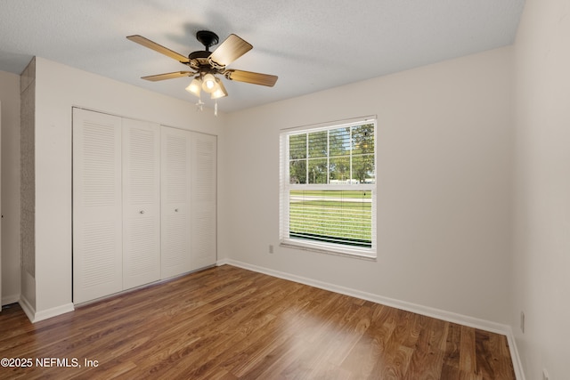 unfurnished bedroom featuring a textured ceiling, a closet, wood finished floors, and baseboards