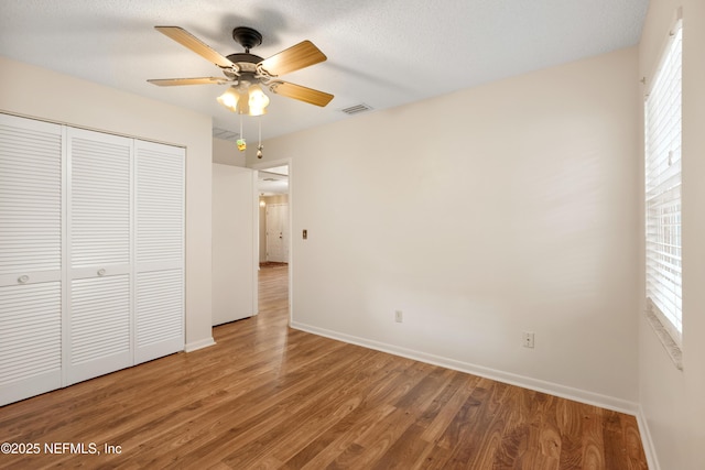 unfurnished bedroom with a closet, visible vents, ceiling fan, wood finished floors, and baseboards