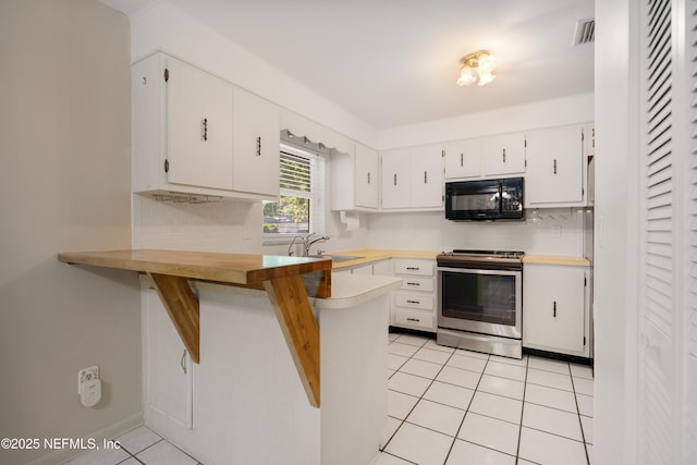 kitchen featuring electric stove, light tile patterned floors, a sink, black microwave, and a peninsula