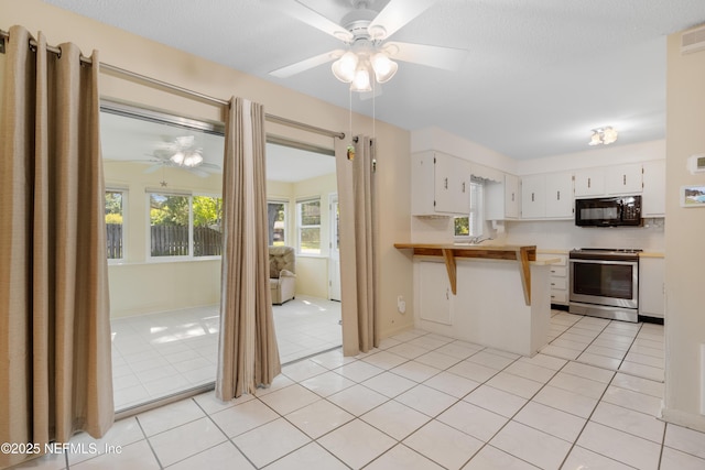 kitchen featuring stainless steel electric range oven, light tile patterned floors, white cabinetry, black microwave, and a peninsula