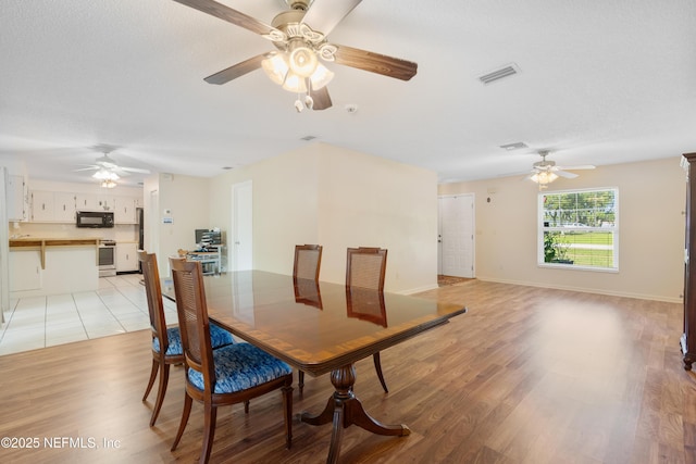 dining area featuring light wood-style flooring, a textured ceiling, visible vents, and baseboards