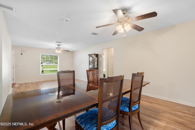 dining space featuring light wood-type flooring, baseboards, visible vents, and a textured ceiling