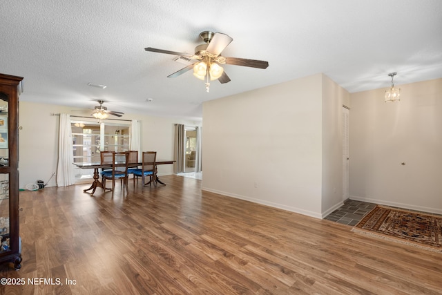 dining area featuring a textured ceiling, wood finished floors, plenty of natural light, baseboards, and ceiling fan with notable chandelier