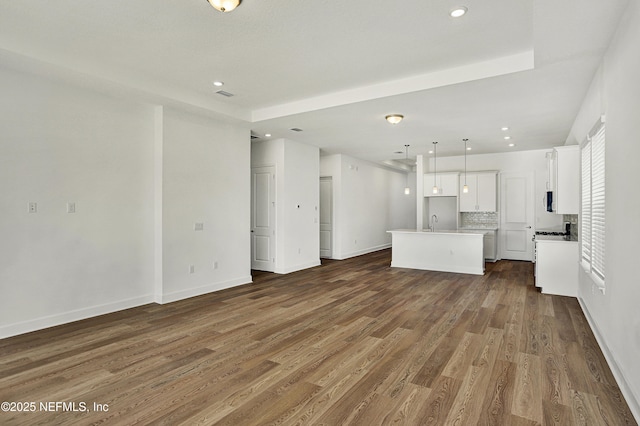 unfurnished living room with visible vents, baseboards, dark wood-style flooring, a sink, and recessed lighting