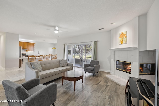 living area featuring baseboards, visible vents, a ceiling fan, a tile fireplace, and a textured ceiling