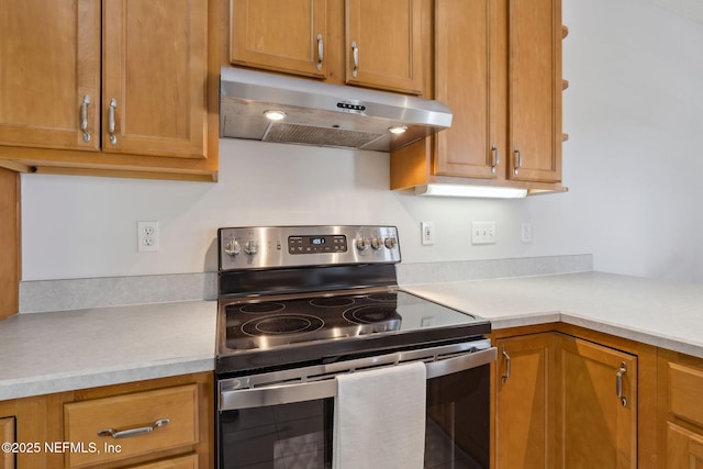 kitchen with brown cabinets, electric stove, light countertops, and under cabinet range hood